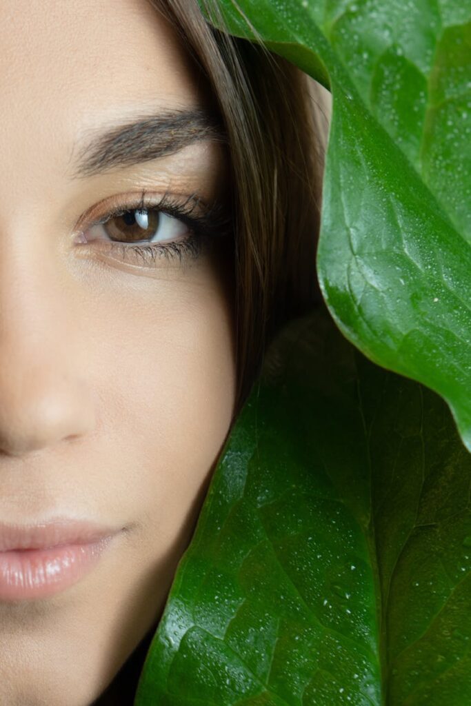 close up photo of a woman s face beside green leaves